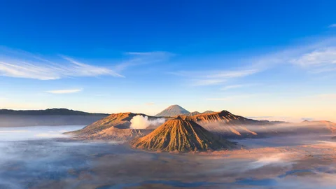 Sunrise over Mount Bromo crater Trekking through volcanic sand in East Java Jeep approaching Penanjakan viewpoint at dawn Golden savanna fields near Mount Bromo