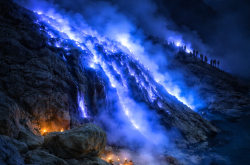 Blue fire phenomenon at Mount Ijen volcano during a midnight hike, East Java, Indonesia, with glowing blue flames and hikers watching before sunrise.
